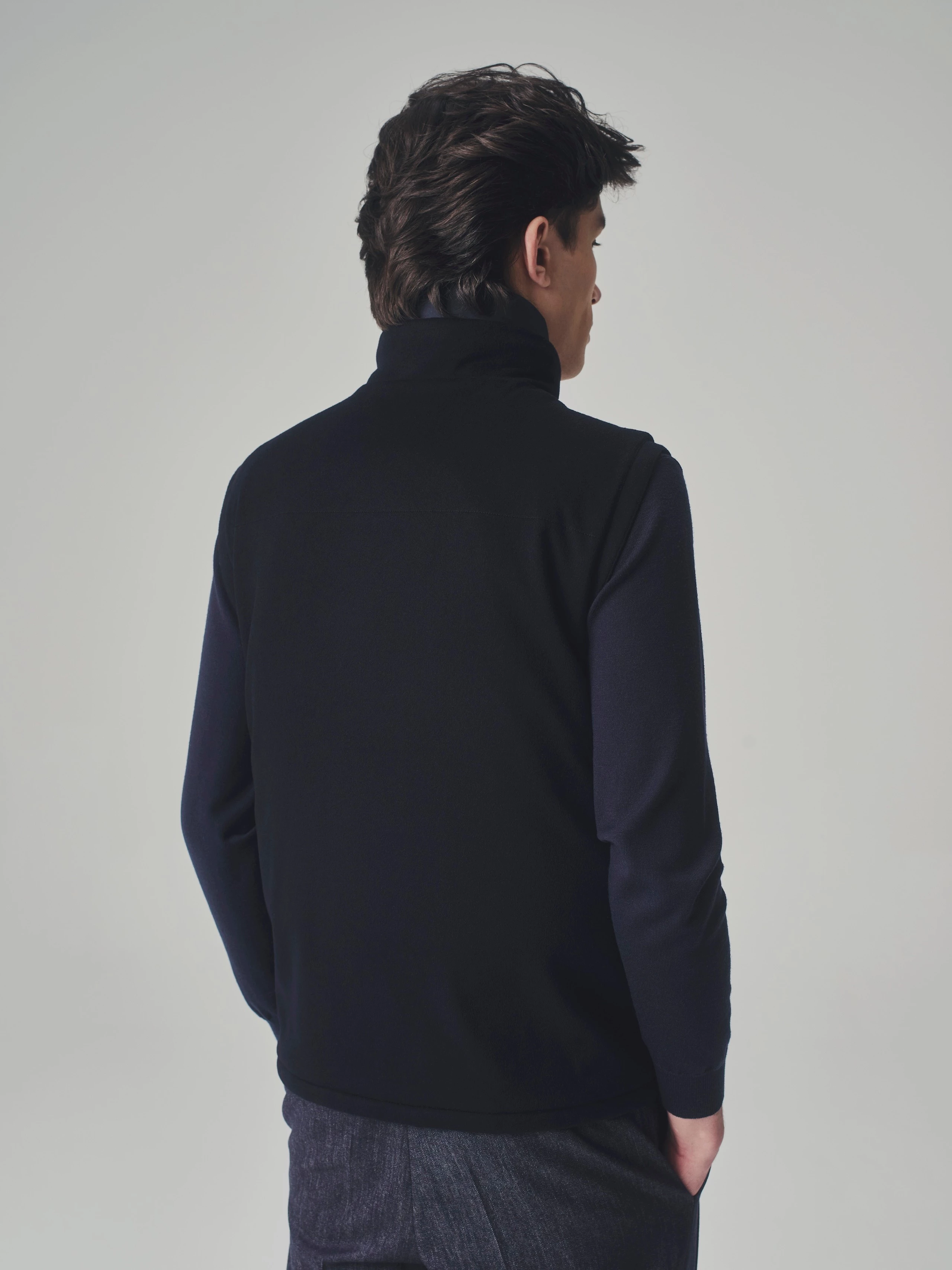 Close-up in a studio: back view of a dark blue cashmere bulletproof vest, cashmere sweater and pleated trousers.
