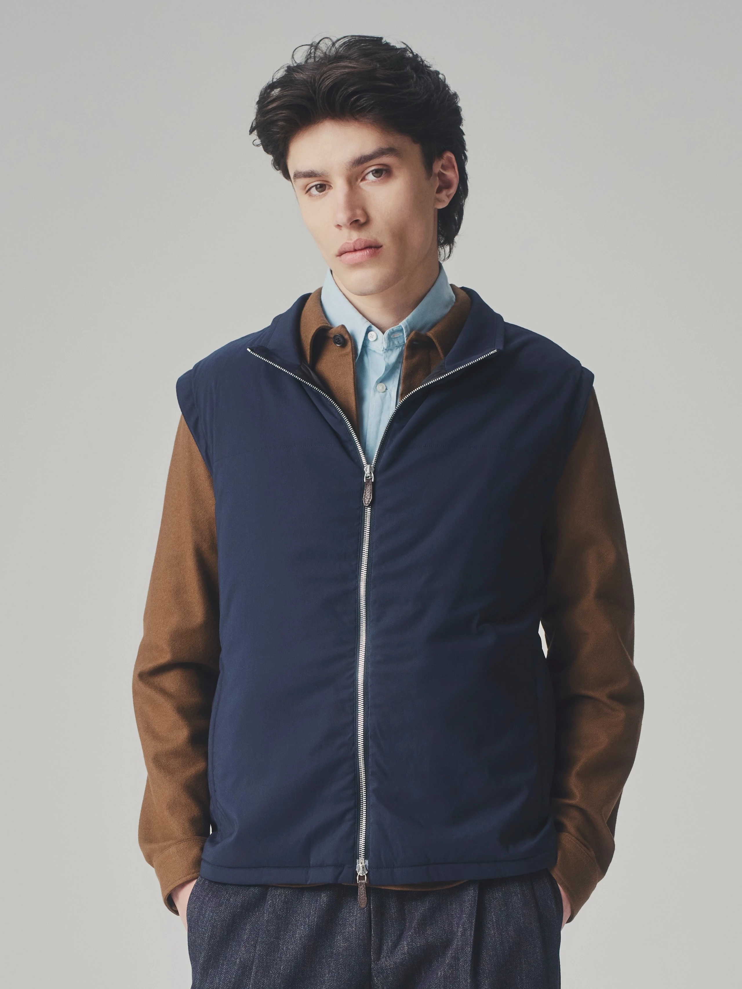 Portrait of a man in a studio wearing a dark blue T-Way bulletproof vest over a brown jacket and light blue shirt.